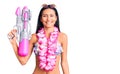 Young beautiful latin girl wearing bikini and hawaiian lei holding water gun looking positive and happy standing and smiling with Royalty Free Stock Photo