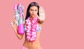 Young beautiful latin girl wearing bikini and hawaiian lei holding water gun with open hand doing stop sign with serious and Royalty Free Stock Photo