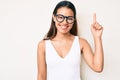 Young beautiful latin girl wearing casual clothes and glasses smiling with an idea or question pointing finger up with happy face, Royalty Free Stock Photo