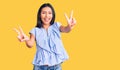 Young beautiful latin girl wearing casual clothes smiling with tongue out showing fingers of both hands doing victory sign Royalty Free Stock Photo