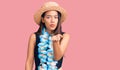 Young beautiful latin girl wearing hawaiian lei and summer hat looking at the camera blowing a kiss with hand on air being lovely Royalty Free Stock Photo