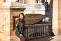 Young, beautiful, Latin and South American woman with leather jacket and top and jeans leaning against a brick wall, looking Royalty Free Stock Photo