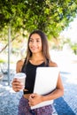 Young beautiful latin student with laptop and cup of coffee studying in the park. Girl is walking in the park with great smile and Royalty Free Stock Photo