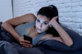 Bored and tired pretty young woman using mobile phone in bed. Royalty Free Stock Photo