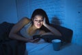 Young beautiful Latin woman on bed late at night texting using mobile phone sleepy and tired Royalty Free Stock Photo