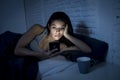 Young beautiful Latin woman on bed late at night texting using mobile phone sleepy and tired Royalty Free Stock Photo