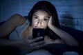 Young beautiful Latin woman on bed late at night texting using mobile phone sleepy and tired Royalty Free Stock Photo