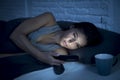 Young beautiful Latin woman on bed late at night texting using mobile phone tired falling sleep Royalty Free Stock Photo