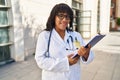 Young beautiful latin woman doctor smiling confident holding clipboard at hospital Royalty Free Stock Photo