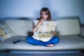 Young beautiful latin woman fully concentrated watching intense movie at night eating popcorn sitting at home sofa couch late nigh Royalty Free Stock Photo