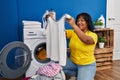 Young beautiful latin woman holding t shirt washing clothes at laundry room