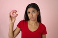 Young beautiful latin woman in red with pink sugar donut thinking and feeling guilty after biting Royalty Free Stock Photo