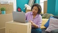 Young beautiful latin woman using laptop sitting on sofa at new home Royalty Free Stock Photo