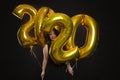 Young beautiful laughing woman with golden balloons in the shape of numbers of the new year. Bright brunette with curly hair and