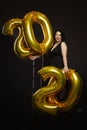 Young beautiful laughing woman with golden balloons in the shape of numbers of the new year. Bright brunette with curly hair and