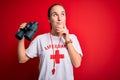 Young beautiful lifeguard woman wearing t-shirt with red cross and whistle using binoculars serious face thinking about question,