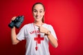 Young beautiful lifeguard woman wearing t-shirt with red cross and whistle using binoculars very happy pointing with hand and
