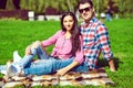 Young beautiful loving couple in checked shirts, jeans and sunglasses sittting on the green lawn