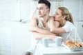 Young beautiful loving couple sitting at the table in the kitchen at home and looking at the window while having breakfast Royalty Free Stock Photo