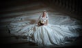 Young beautiful luxurious woman in wedding dress sitting on stair steps in semi-darkness. Bride with huge wedding dress Royalty Free Stock Photo