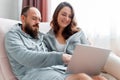 Young beautiful married couple are sitting on sofa at home interior using laptop. Happy smiling Woman and man do Royalty Free Stock Photo