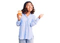 Young beautiful mixed race woman drinking a coffee from take away cup pointing thumb up to the side smiling happy with open mouth Royalty Free Stock Photo