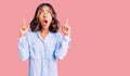 Young beautiful mixed race woman wearing casual business shirt amazed and surprised looking up and pointing with fingers and Royalty Free Stock Photo