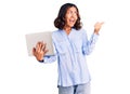 Young beautiful mixed race woman working using computer laptop pointing thumb up to the side smiling happy with open mouth Royalty Free Stock Photo