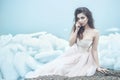 Young beautiful model in luxurious strapless corset ball gown sitting on slabs of broken ice at the misty seaside