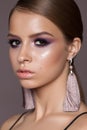 Young beautiful model with a professional colorful make up, hazel eyes, smooth hairstyle and fashion brushes earrings.