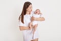 Young beautiful mother with cute little crying baby posing isolated over white background, mommy calm down her daughter, lady Royalty Free Stock Photo