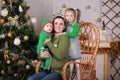 Young beautiful mother with her baby son in elf costume and little girl sitting in rocking chair near christmas tree. Royalty Free Stock Photo