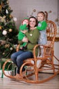 Young beautiful mother with her baby son in elf costume and little girl sitting in rocking chair near christmas tree Royalty Free Stock Photo