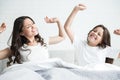 Young beautiful mother and her cute teen daughter just woke up together sitting in bed stretching Royalty Free Stock Photo