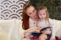 Young beautiful mother with her little daughter reading a book sitting on the couch. Royalty Free Stock Photo