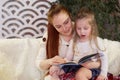 Young beautiful mother with her little daughter reading a book sitting on the couch. Royalty Free Stock Photo
