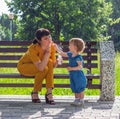 a young beautiful mother and her little daughter sit happy on a bench in the Park and blow soap bubbles Royalty Free Stock Photo