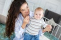 Young beautiful mother holding baby son on her lap, sitting on a bed Royalty Free Stock Photo