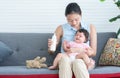 Young beautiful mother holding and feeding milk to cute little Caucasian 7 months newborn baby, sitting together on sofa at home Royalty Free Stock Photo