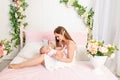 A young beautiful mother holds her daughter a girl of 6 months on her lap on a white bed, playing and kissing her, place for text Royalty Free Stock Photo