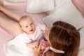 A young beautiful mother holds her daughter a girl of 6 months on her lap on a white bed, playing and kissing her, place for text Royalty Free Stock Photo