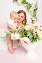 A young beautiful mother holds her daughter a girl of 6 months on a white bed and looks at flowers, a place for text Royalty Free Stock Photo