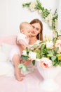 A young beautiful mother holds her daughter a girl of 6 months on a white bed and looks at flowers, a place for text Royalty Free Stock Photo