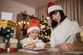 Young beautiful mother and little cute child daughter in red hats writing letter to Santa Claus Royalty Free Stock Photo