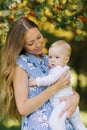 A young beautiful mother with long blond hair holds a 10-month-old baby in her arms, looks at him and smile Royalty Free Stock Photo