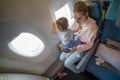 Young beautiful mother is sitting in an airplane chair, her little cute baby is sitting in her arms and looking out the Royalty Free Stock Photo