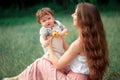 Young beautiful mother sitting with her little son against green grass. Happy woman with her baby boy on a summer sunny Royalty Free Stock Photo