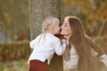 A young beautiful mother in a sweater and her cute daughter are having fun on a walk in the autumn Park. Mom plays with