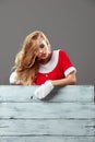 Young and beautiful mrs.Santa Claus dressed in the red robe and gloves stands behind a white wooden fence and leans on Royalty Free Stock Photo