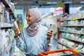 A young beautiful Muslim woman in a hijab chooses a product for washing hair, a shampoo, a conditioner, a woman holds a